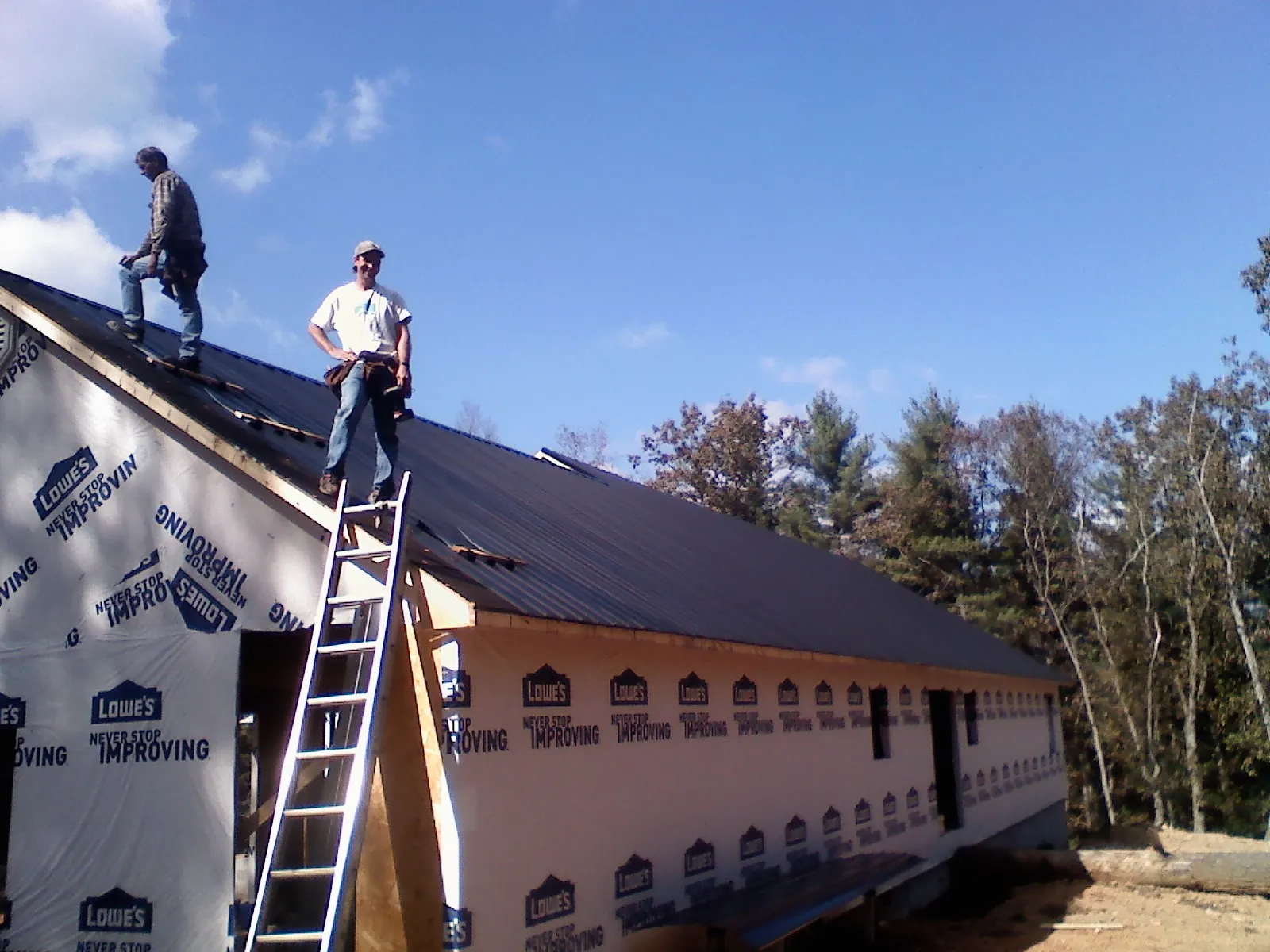 Two roofers standing on a long dark metal roof over a wrapped building in Liberty