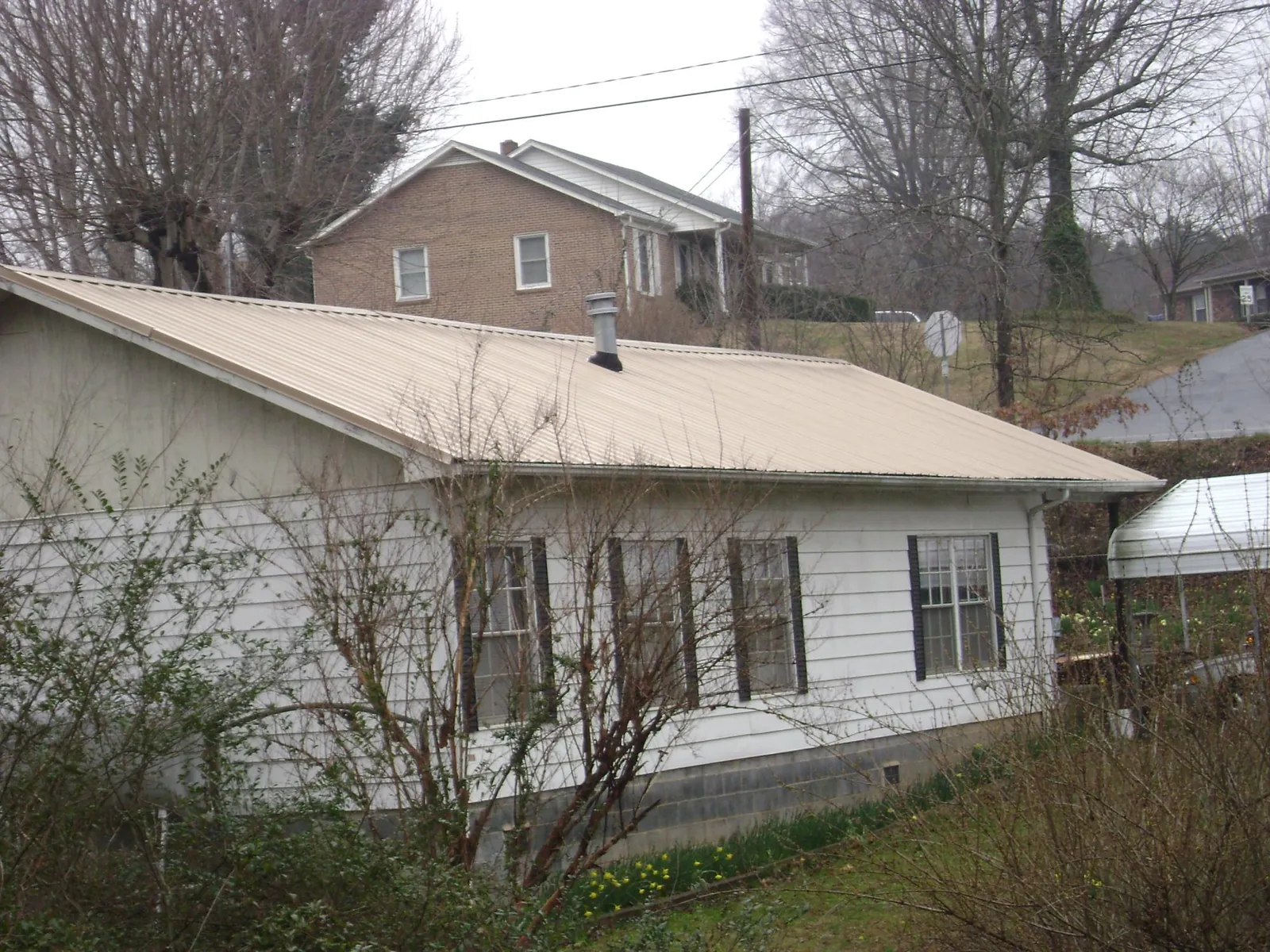 Tan metal roof on a white sided house set into a hillside — Commercial Roofing by Roofing Brothers in Liberty